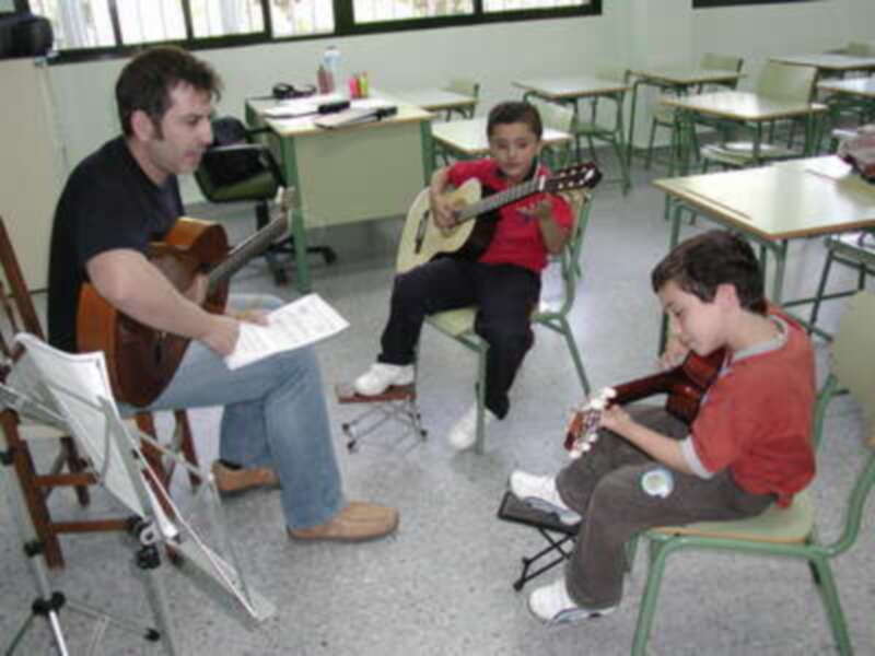 Maestro enseñando guitarra a estudiantes en una clase de música escolar.