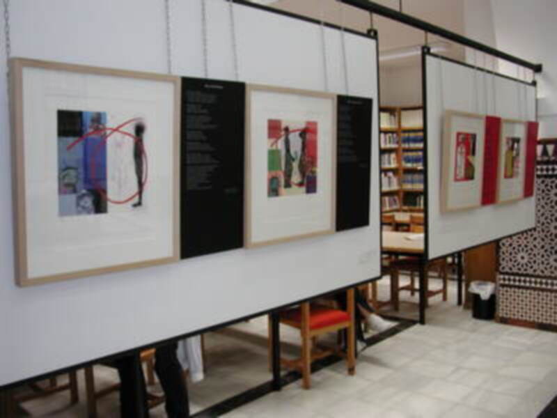 Exposición de arte enmarcado colgando en una biblioteca, con textos explicativos y obras de arte visibles.