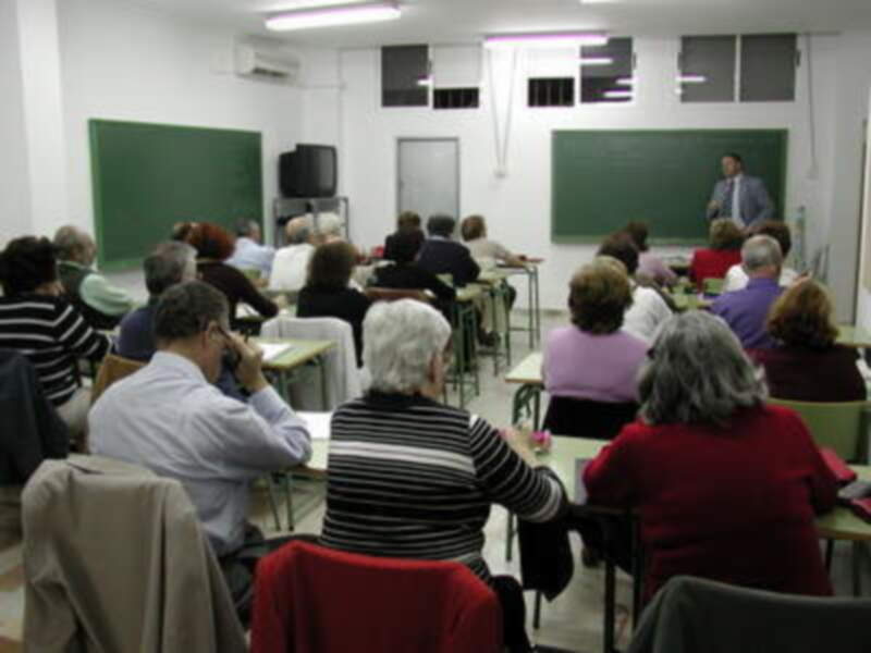 Clase de adultos en un aula con pizarras y profesor explicando.