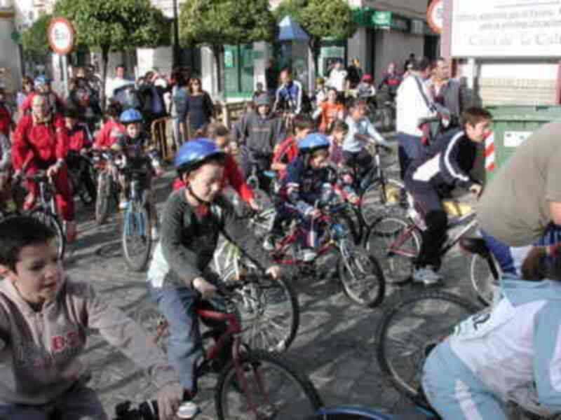 Grupo de niños en una carrera de bicicletas en la calle, con adultos supervisando.