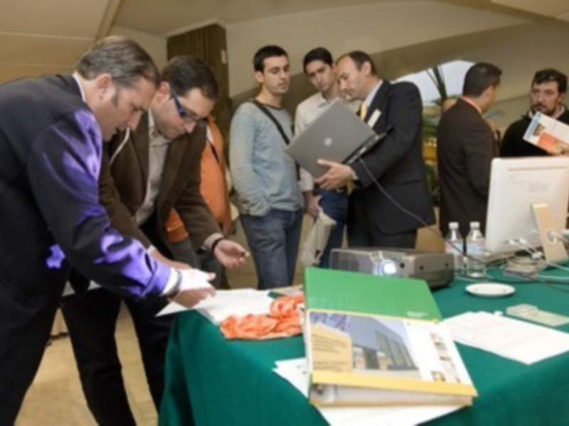 Exposición de tecnología con participantes interactivos observando un dispositivo en una mesa.