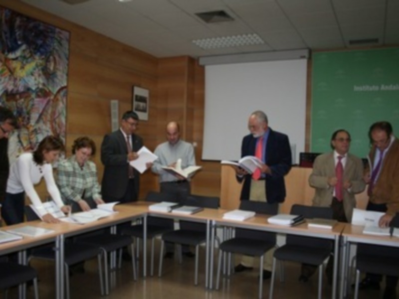 Una reunión formal en una sala de conferencias con personas sentadas en mesas y discutiendo documentos.