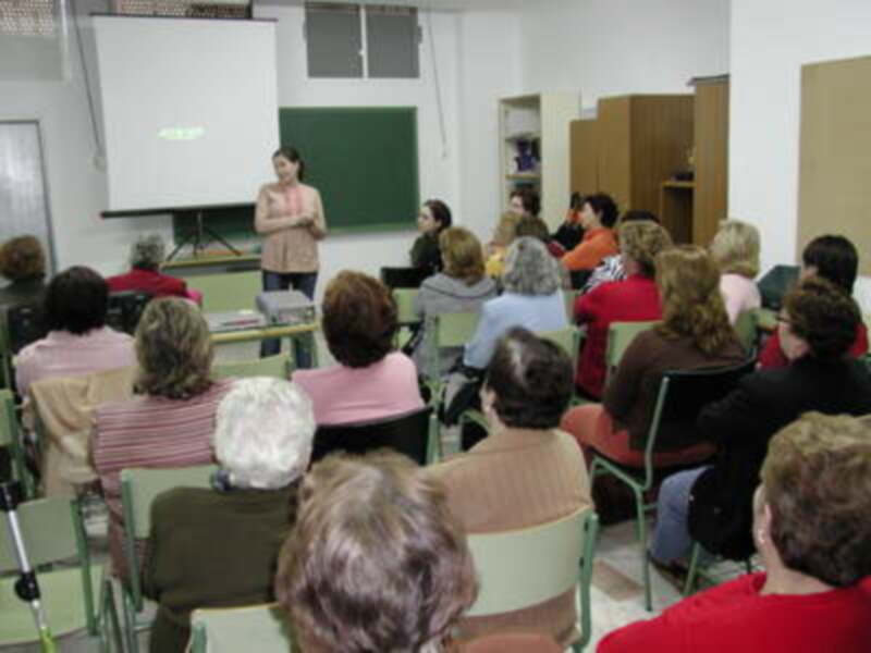 Una clase de educación ambiental en un aula con una maestra explicando a un grupo de estudiantes. La sala está equipada con una pizarra, una proyección y sillas para los estudiantes. La maestra está usando un gesto para explicar algo importante.