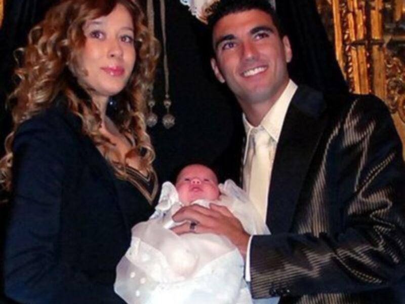 Una familia feliz con su recién nacido, todos sonrientes y vestidos formalmente.