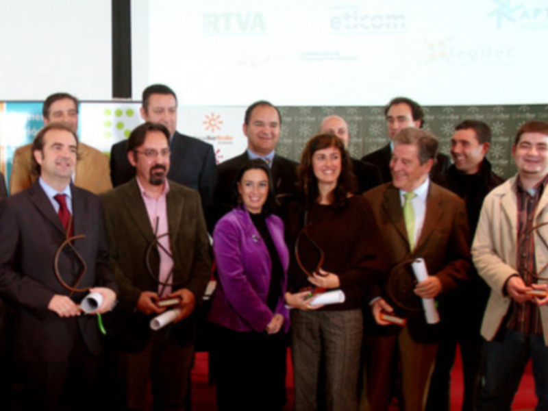 Una reunión de empresarios en un evento de reconocimiento empresarial, con un fondo de proyección que muestra logos de empresas. Los participantes están sonriendo y posando para la foto, con algunos de ellos sosteniendo premios o reconocimientos.
