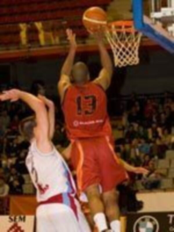 Jugador en rojo realiza un mate durante un partido de baloncesto.