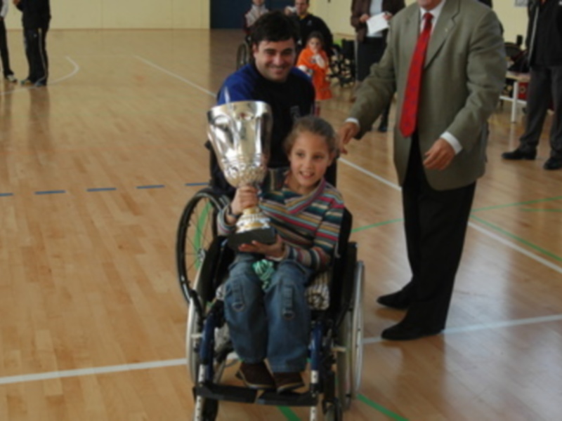 Niño en silla de ruedas celebrando con un trofeo en una cancha deportiva.