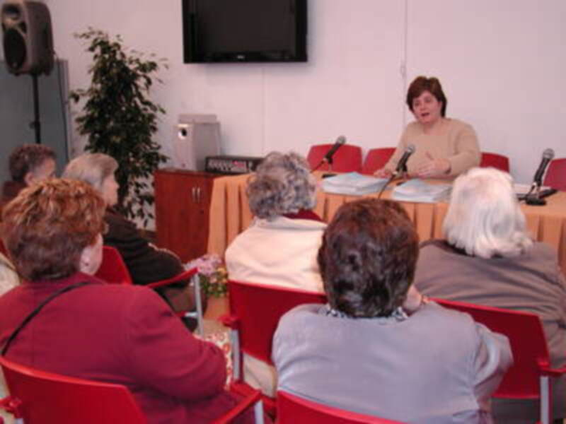 Reunión informativa con una presentadora hablando a un grupo de asistentes sentados en una sala de conferencias.