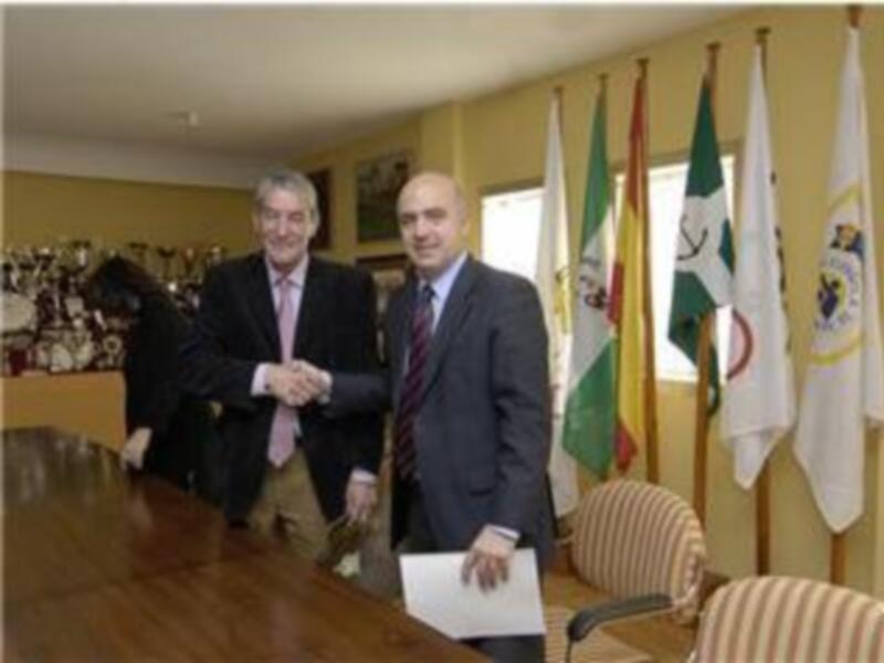 Dos hombres en traje se saludan en una reunión formal en un entorno profesional con banderas y un escritorio de madera.