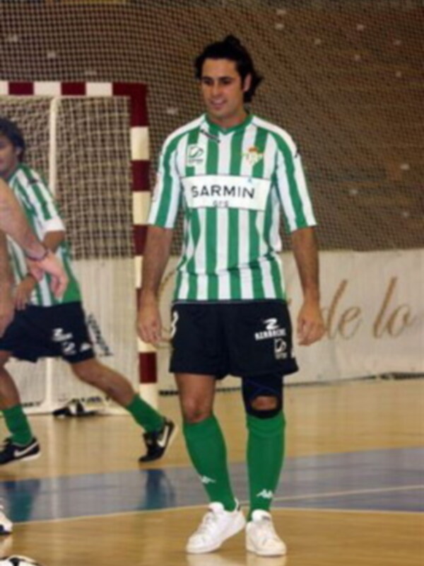 Jugador de fútbol sala en uniforme verde y blanco, con detalles de patrocinio, en un partido en un pabellón deportivo.