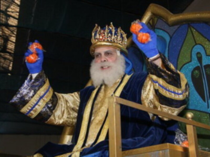 Figura vestida de rey con corona dorada, sosteniendo mandarinas, sentado en un trono dorado.