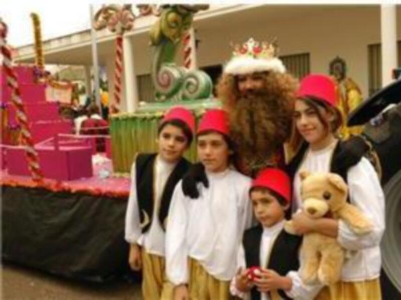 Desfile de carrozas navideñas con niños vestidos de los Reyes Magos y un personaje de la historia de la Navidad.