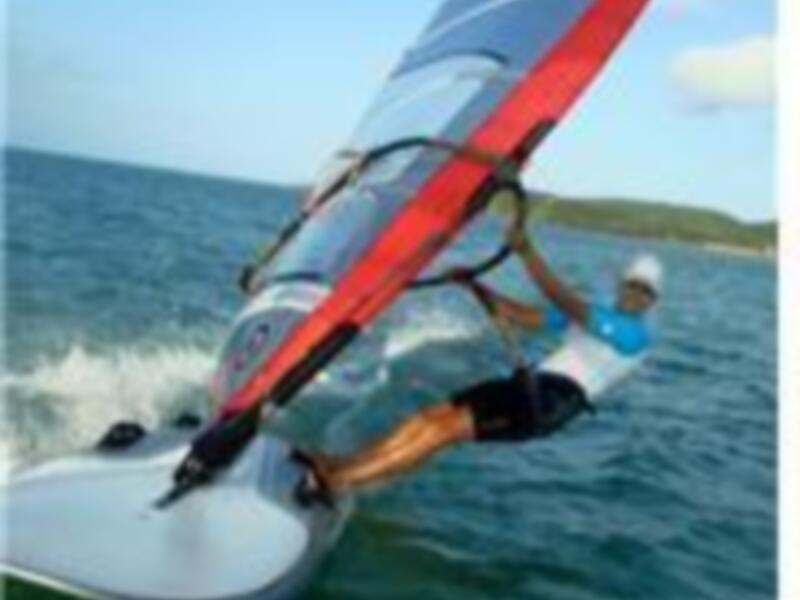 Vela de windsurf en acción sobre el agua azul con un cielo azul claro.