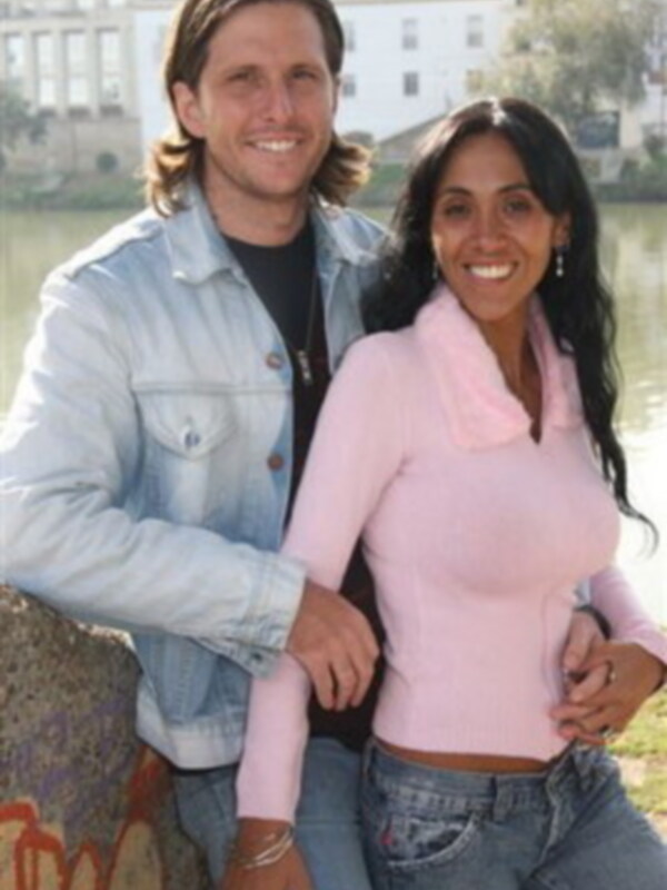 Una pareja sonríe juntos en un entorno urbano junto a un río.