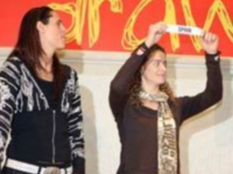 Dos mujeres interactúan en un evento, una sostiene un objeto blanco mientras la otra observa.