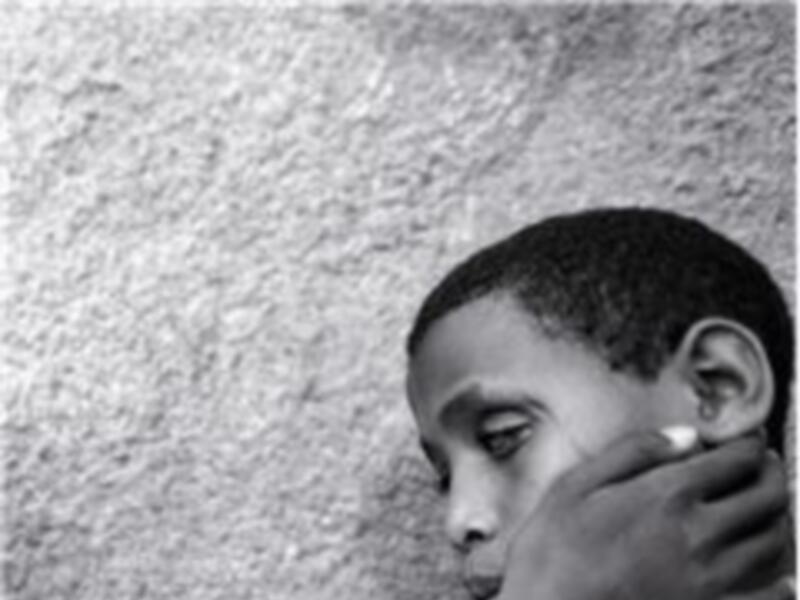 Niño reflexivo apoyado en una pared, retrato en blanco y negro.