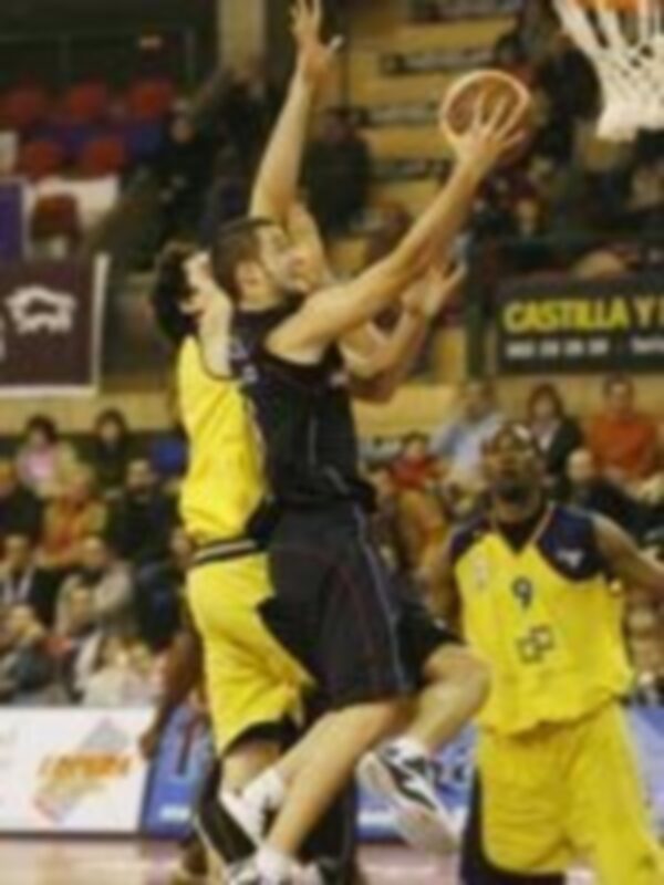 Jugador en acción durante un partido de baloncesto, intentando hacer un tiro mientras es defendido por un oponente.