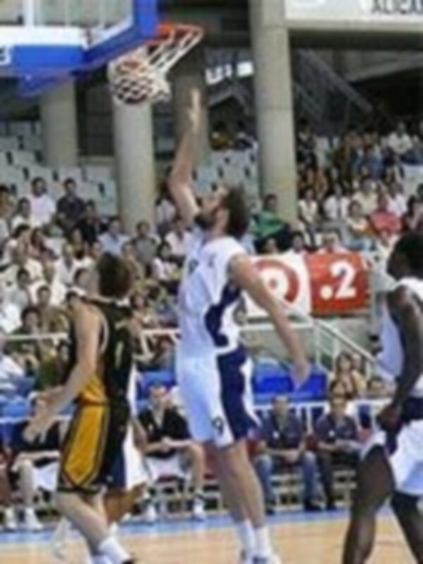 Jugador en acción durante un partido de baloncesto, lanzando al aro en un estadio lleno de espectadores.