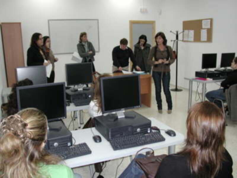 Clase de informática con estudiantes y profesora en un aula equipada con computadoras.