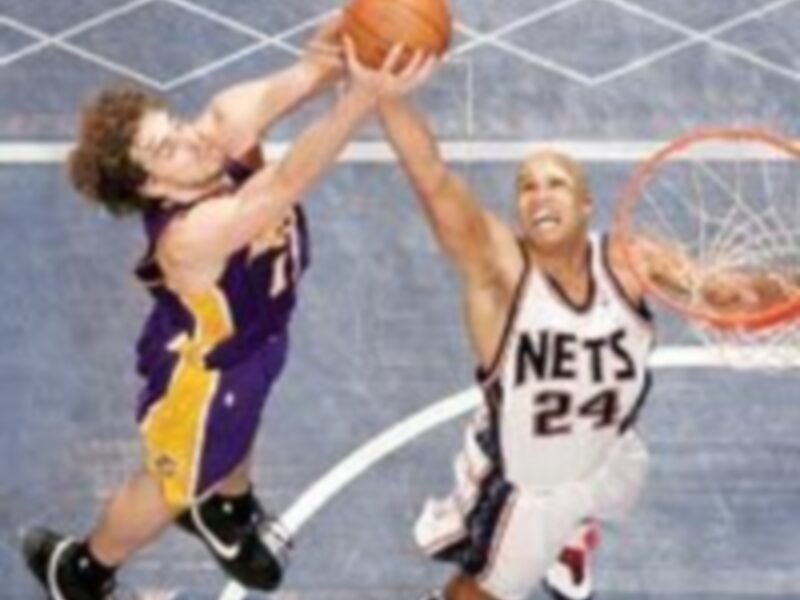 Juego de baloncesto entre Lakers y Nets, con un jugador de Lakers intentando bloquear el tiro de un jugador de Nets.