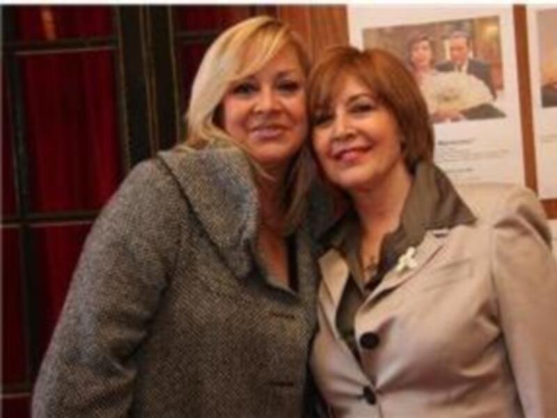 Dos mujeres sonríen juntas en un evento, posando frente a carteles de películas.