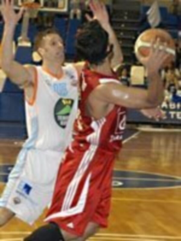 Jugadores en acción durante un partido de baloncesto. Uno en blanco y otro en rojo luchan por el balón.