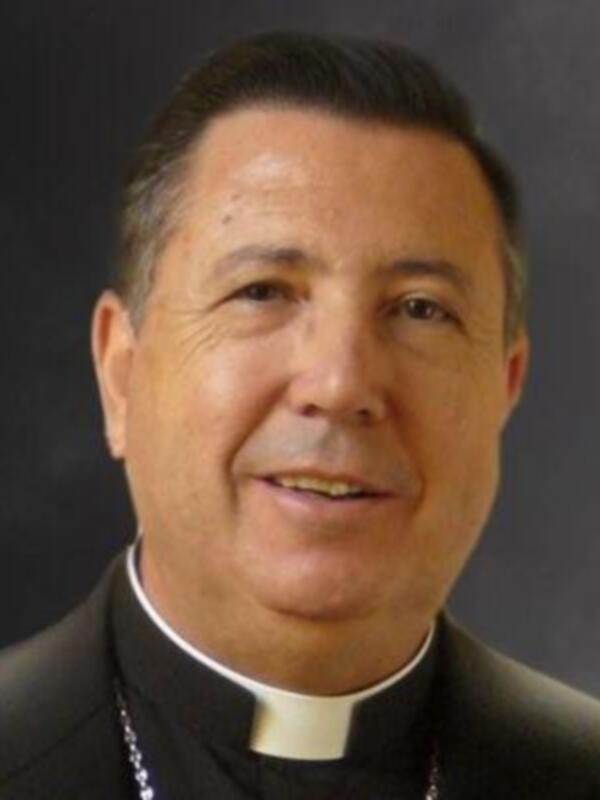 Retrato de un sacerdote con vestimenta clerical, sonriendo.