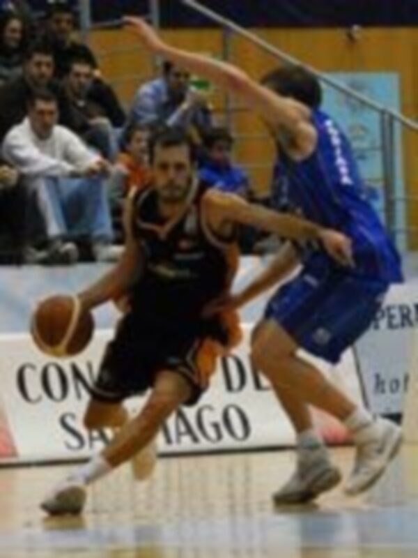 Jugadores de baloncesto en acción durante un partido, uno en negro y otro en azul, disputando el balón en una cancha deportiva.