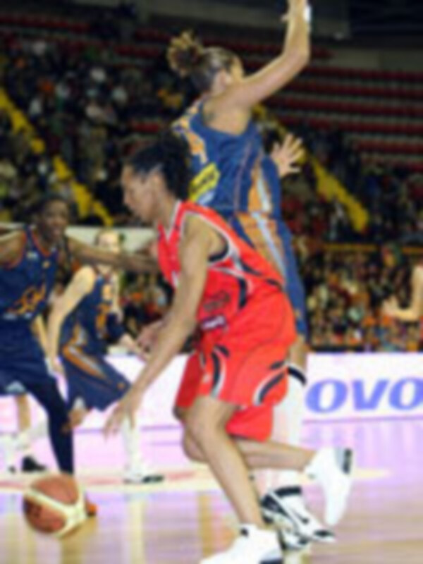 Jugadores de baloncesto en acción durante un partido, uno en rojo y otro en azul, en un entorno deportivo iluminado.