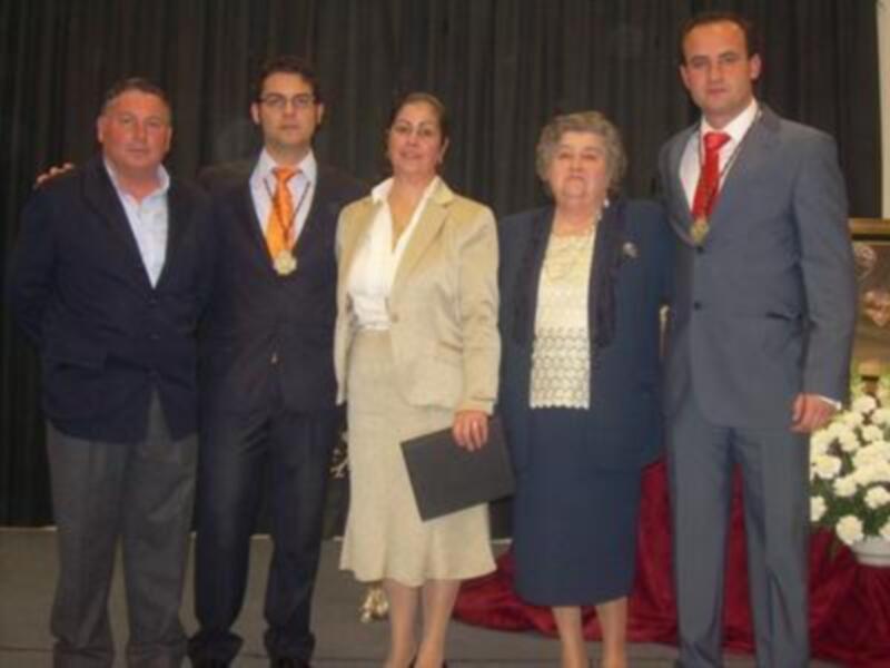 Celebración de un evento formal con cuatro personas en trajes y vestidos formales, posando juntos en un escenario.