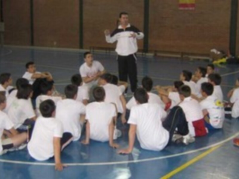 Un instructor de fútbol se dirige a un grupo de jóvenes jugadores sentados en el suelo en una cancha de fútbol, probablemente durante una sesión de entrenamiento o motivación.