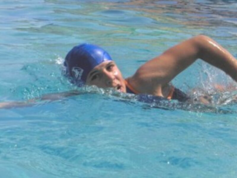 Una persona nadando con estilo de braza en una piscina de agua clara.