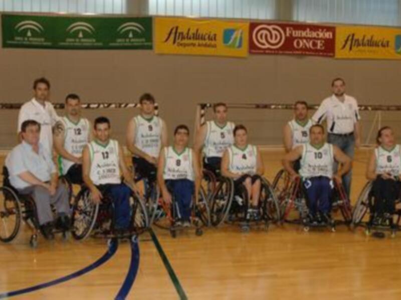 Equipo de baloncesto en silla de ruedas posando en una cancha deportiva.