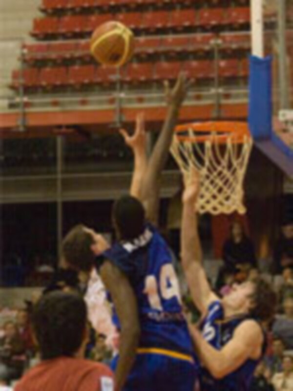 Jugadores de baloncesto en acción durante un partido, con un jugador lanzando el balón hacia el aro.