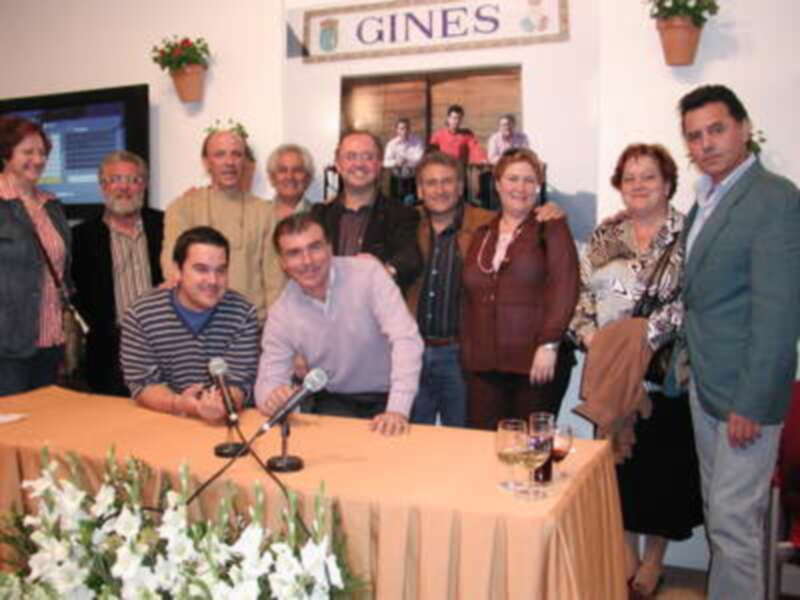 Reunión de personas en una sala con mesas, micrófonos y flores, en un ambiente formal.