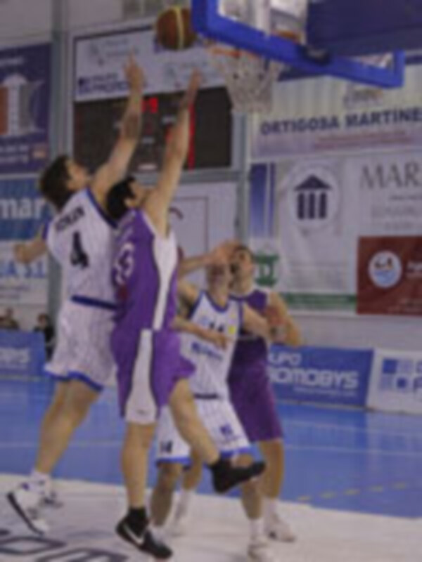 Jugadores de baloncesto en acción durante un partido, con anuncios en el fondo.