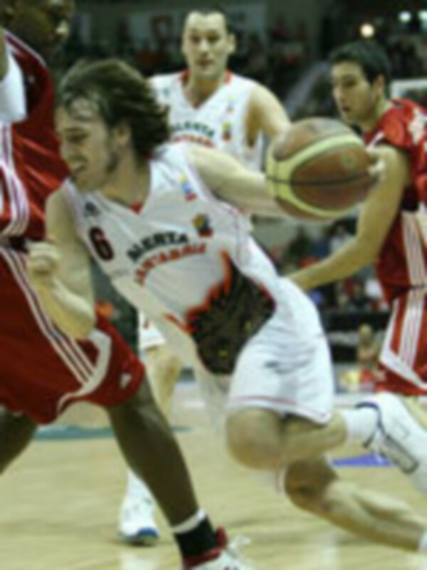 Un jugador de baloncesto en acción durante un partido, con el equipo contrario en el fondo.