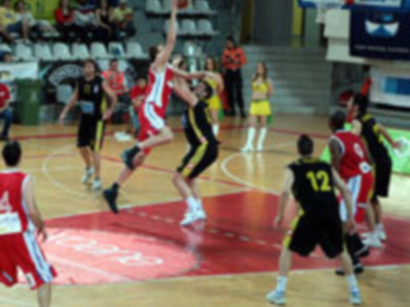 Jugadores de baloncesto en acción durante un partido, con un jugador en rojo saltando para marcar a su oponente en el aro.