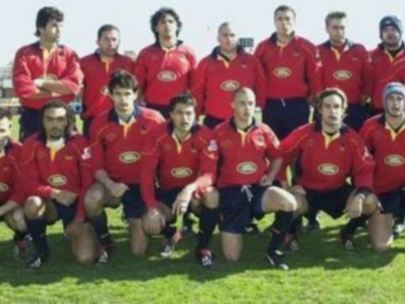Equipo de rugby posando en campo con uniforme rojo y negro, en un día soleado.