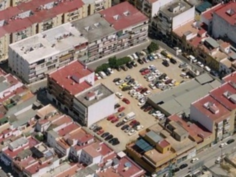 Aerial view of a residential and commercial area with red roofs and various buildings, including a large white building with a flat roof and a smaller building with a red roof and a white awning.