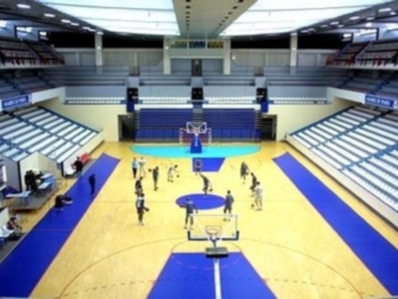 Jugadores de baloncesto en acción en una amplia cancha de baloncesto con gradas vacías alrededor.