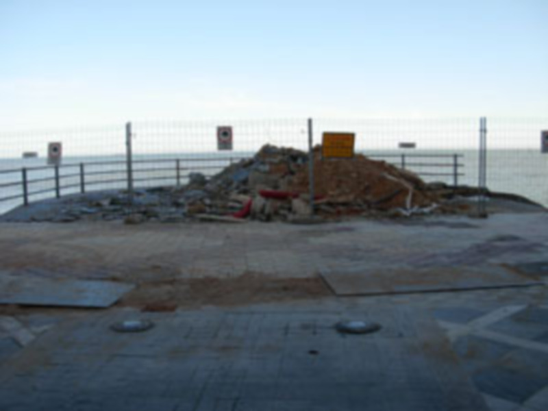 Zona de construcción con montón de escombros y valla de seguridad al borde del mar.