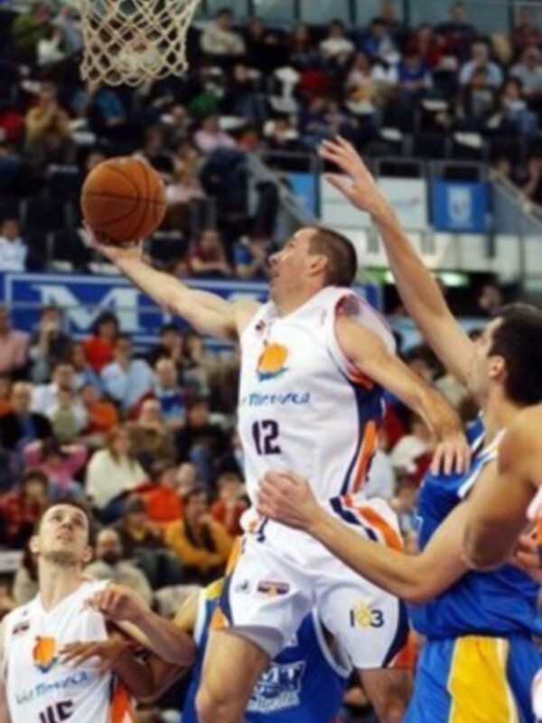 Un jugador de baloncesto en acción, lanzando el balón hacia el aro mientras otros jugadores lo defienden.
