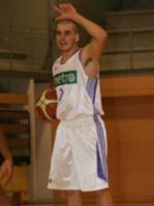 Un jugador de baloncesto en acción, con el balón bajo el brazo izquierdo y la mano derecha levantada, posiblemente en un gesto de celebración o comunicación con su equipo.