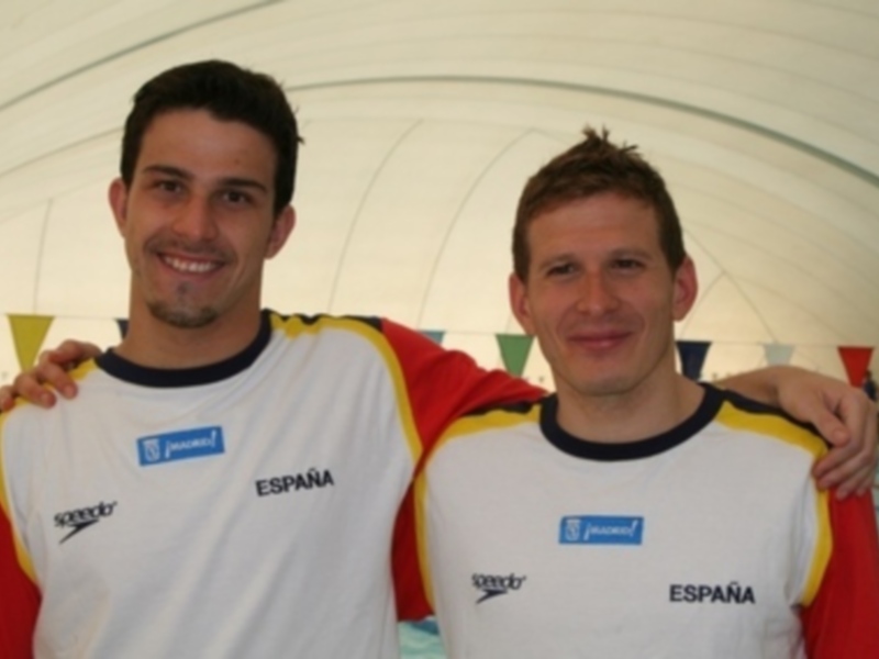 Dos atletas españoles sonrientes en uniforme de natación, posando juntos en un entorno deportivo.