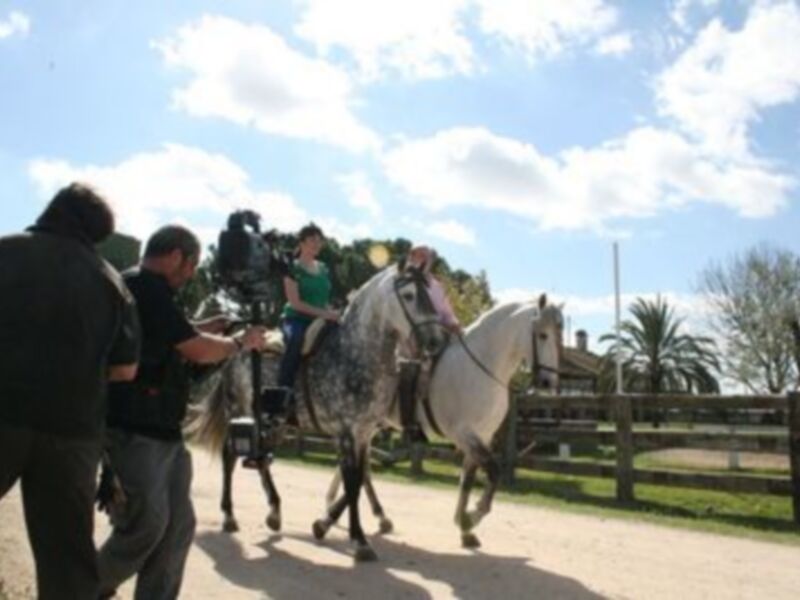 Equipo de filmación grabando una escena con caballos en un entorno rural soleado.