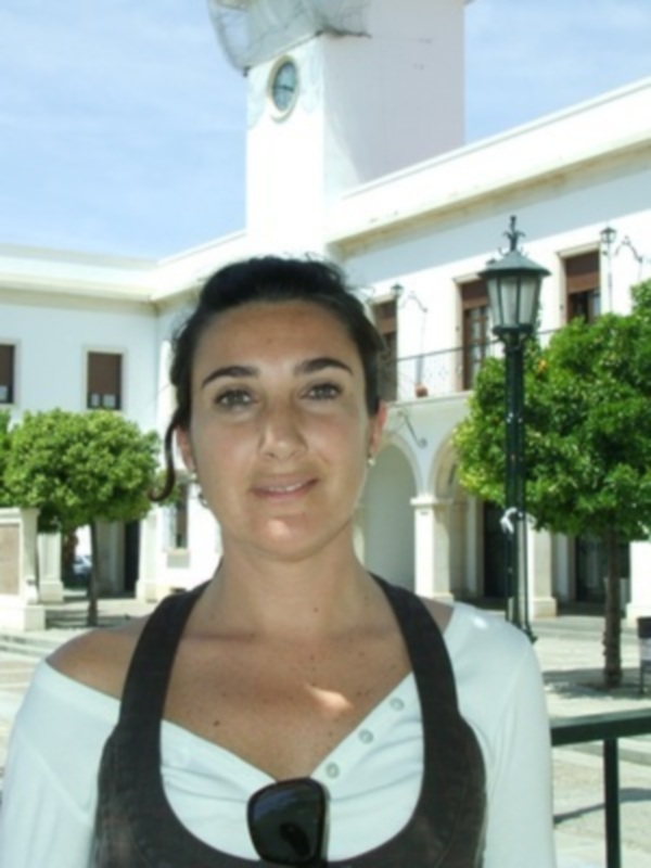 Una mujer joven con una camiseta blanca y negra, posando frente a una estructura con una torre en el fondo.