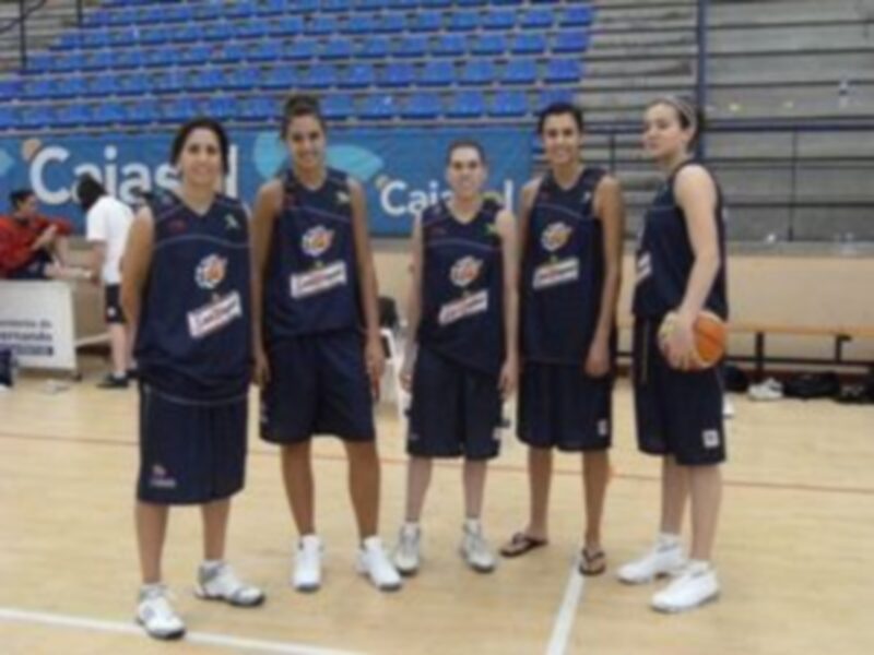 Equipo de baloncesto femenino posando en el gimnasio, con uniformes y balones en la mano. El equipo parece estar listo para un partido o entrenamiento.