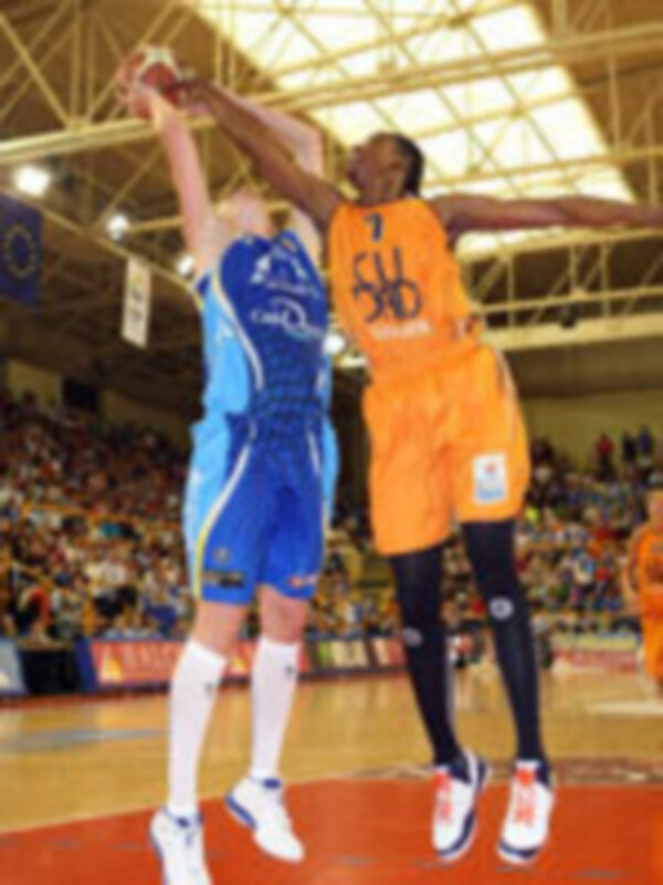 Jugadores de baloncesto en acción durante un partido, uno en azul y otro en naranja, luchando por el balón en el aire.