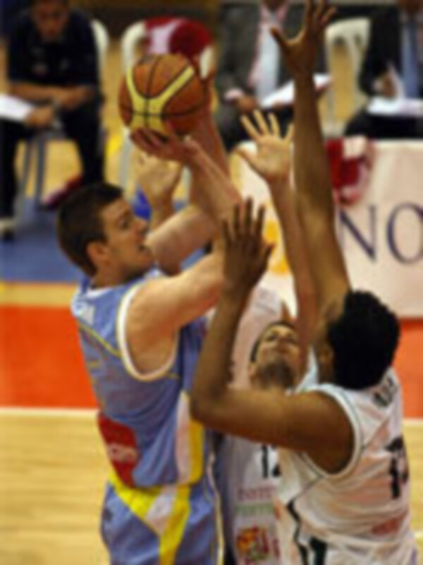 Un emocionante partido de baloncesto en una cancha deportiva, con jugadores en acción y un público entusiasta en el fondo.